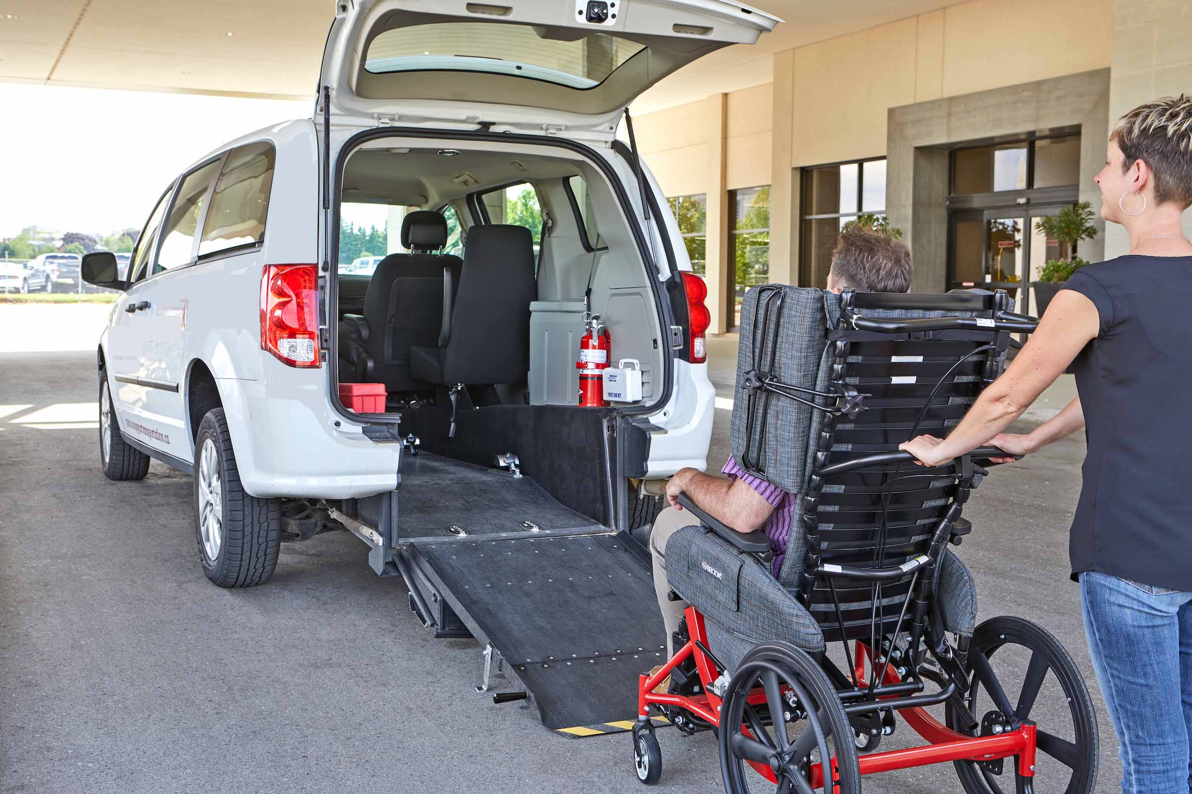 A woman is providing wheelchair transportation services by pushing a wheelchair into a van.