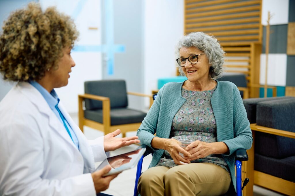 Elderly woman in wheelchair talking to her doctor at medical clinic.