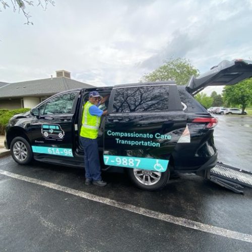 A person stands beside an accessible van with a ramp and "Compassionate Care Transportation" signage, parked in a lot on a cloudy day. This is the perfect choice for those searching for reliable wheelchair transportation services near me.