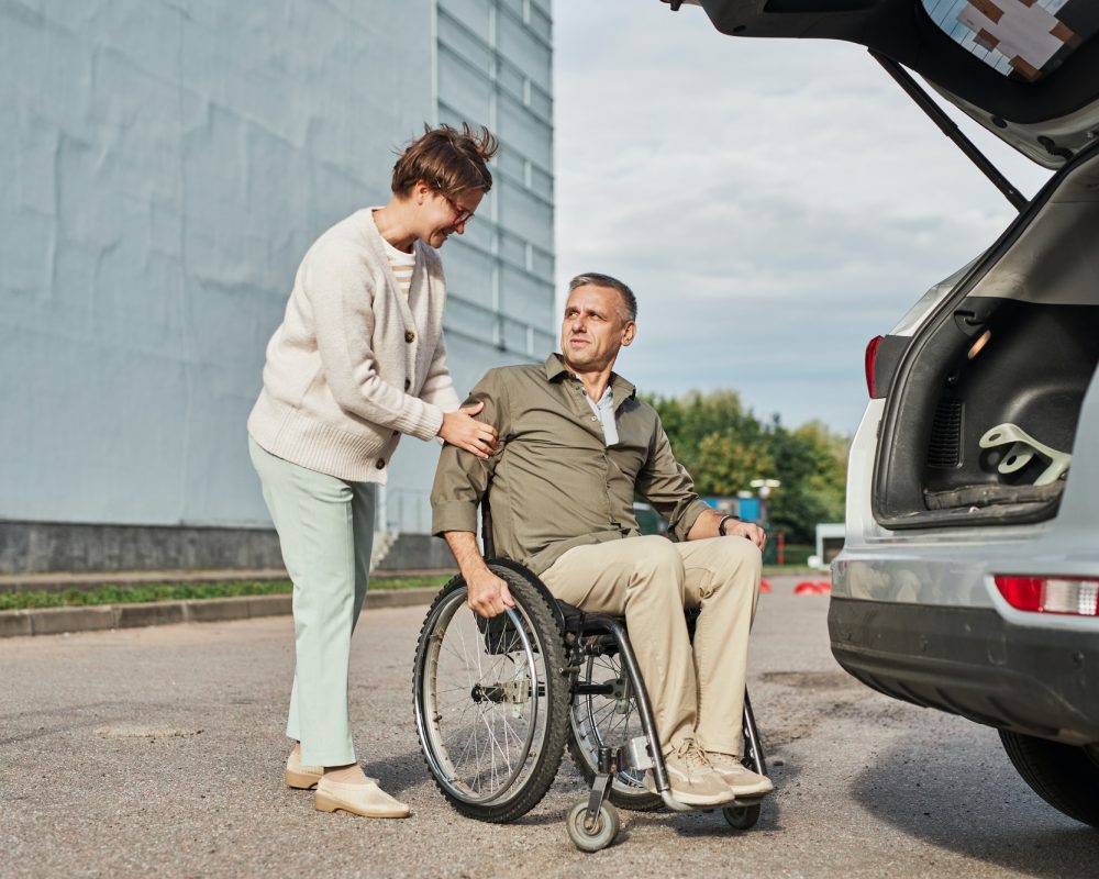A man in a wheelchair is helping a woman open the trunk of a car.
